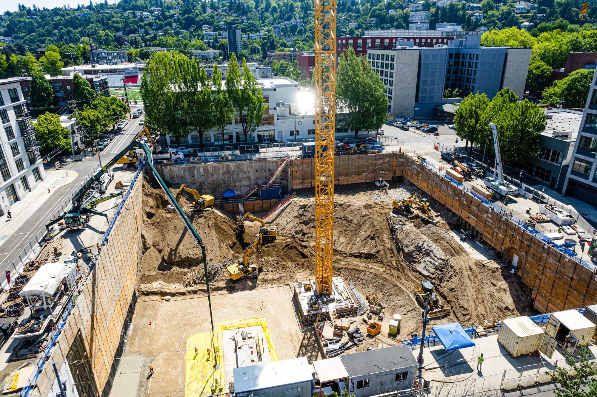 An aerial view of the press blocks construction site with tall wood-lagging shoring walls extending over 60' below ground level. 