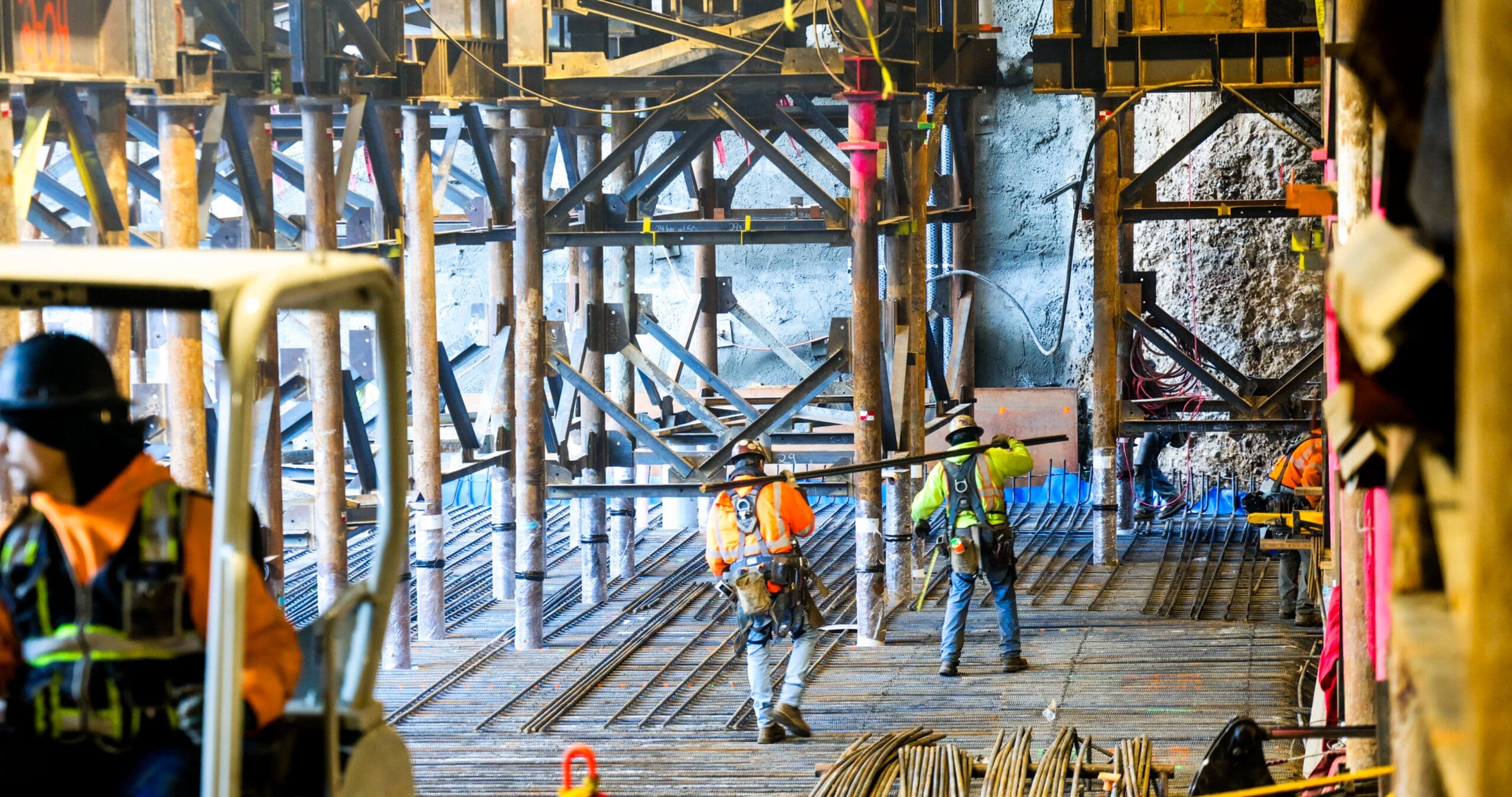Construction workers carry and set rebar amongst micropiles and steel towers
